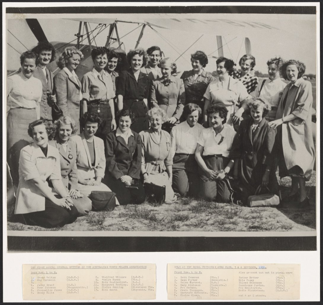 Black and white photo of 21 women of various ages smiling, standing in front of a plane. Below the image is a list of these women's names and where they're from