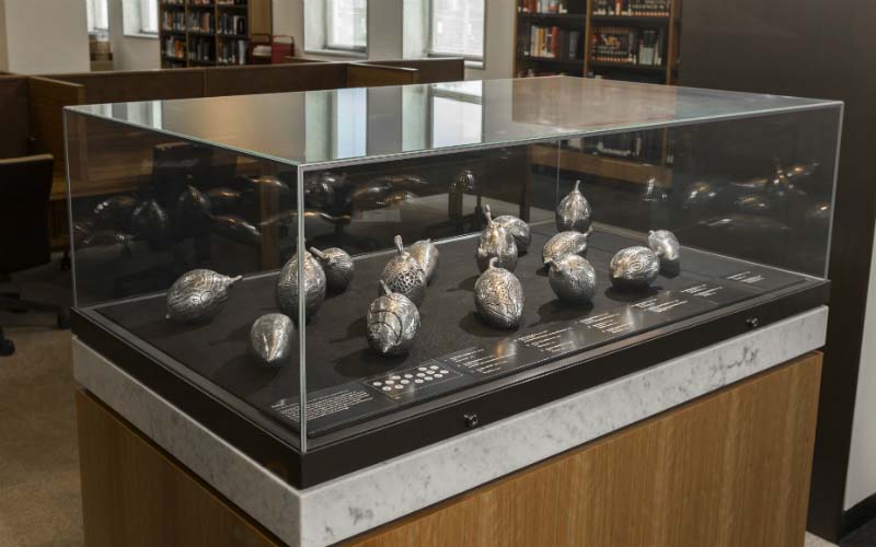 Fifteen small silver sculptures in a glass display case