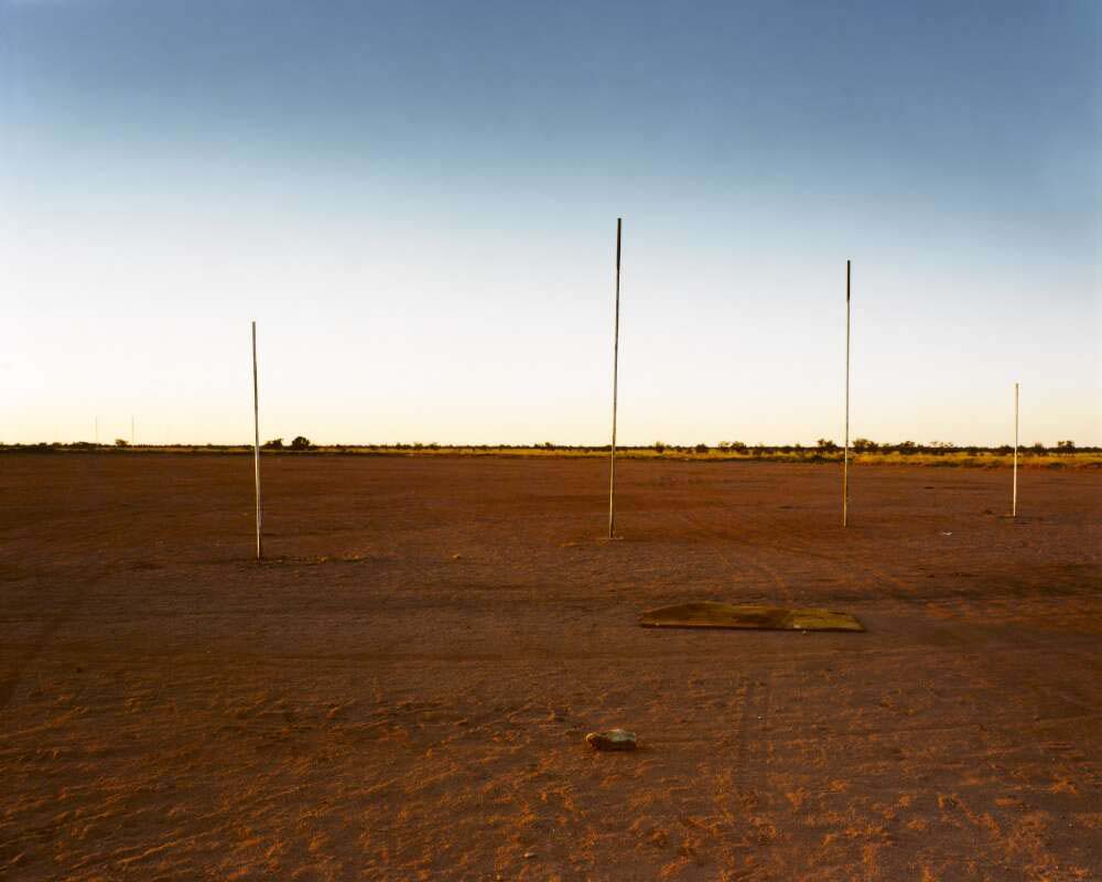 Football goal posts on a red dirt field with a clear blue sky, a single football book abandoned in the front.