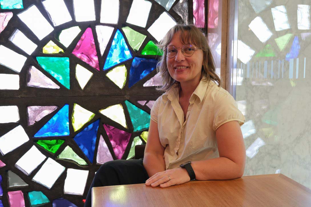 2022 Summer Scholar Deborah Lee-Talbot sitting in front of a stained glass window at the Library