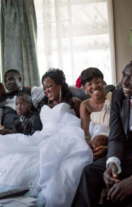 A family dressed for a wedding laughs as they sit together on a couch