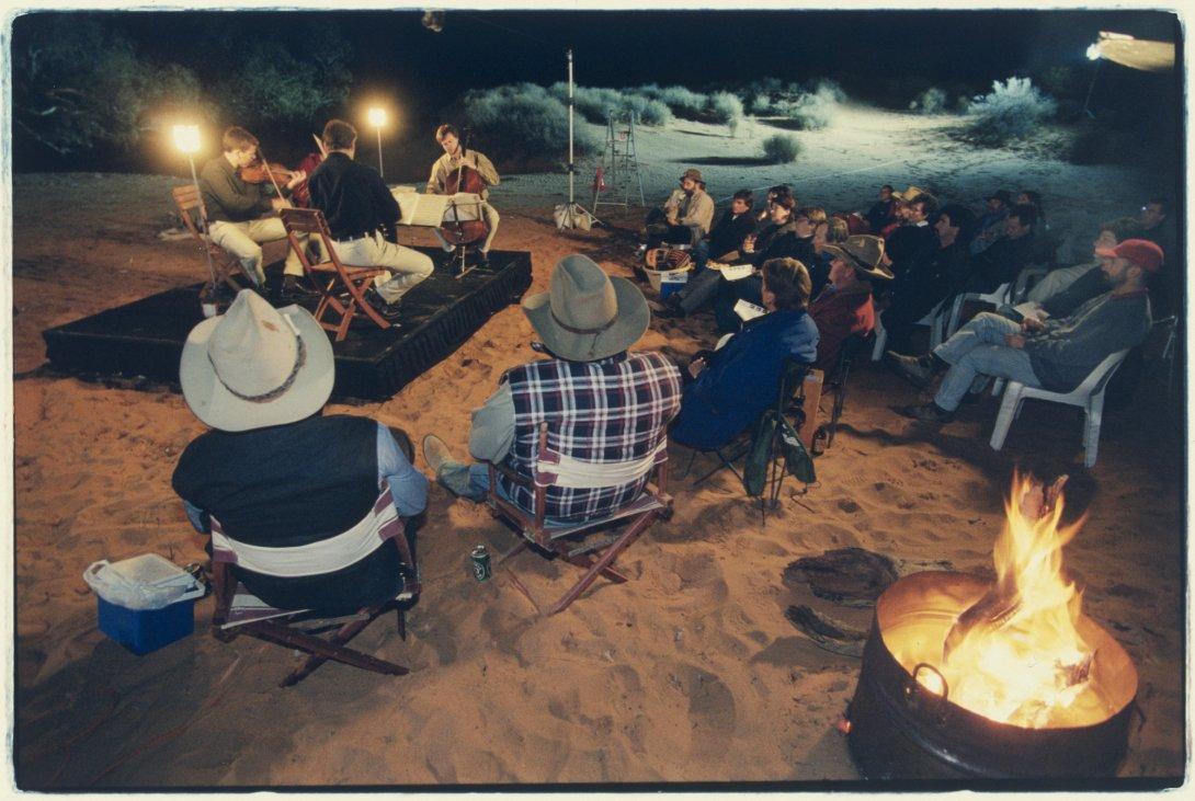 The Australian String Quartet perform on a stage in a dried-up creek bed near the Clayton Station. A small group of audience members are sitting in chairs in front of the stage.