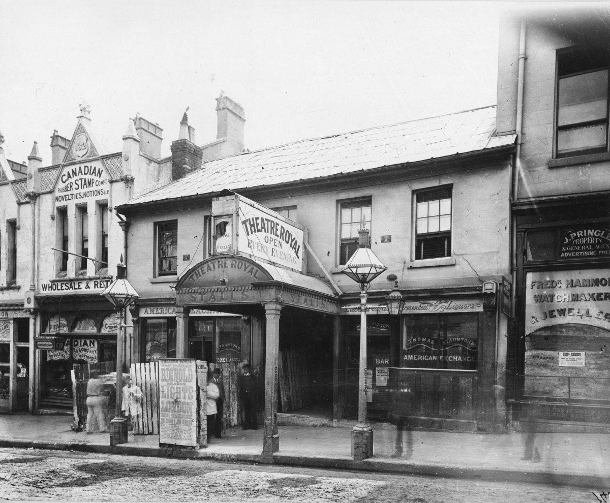 Black and white photograph of a row of shopfronts. One facade reads 'Theatre Royal: Open Every Evening'.