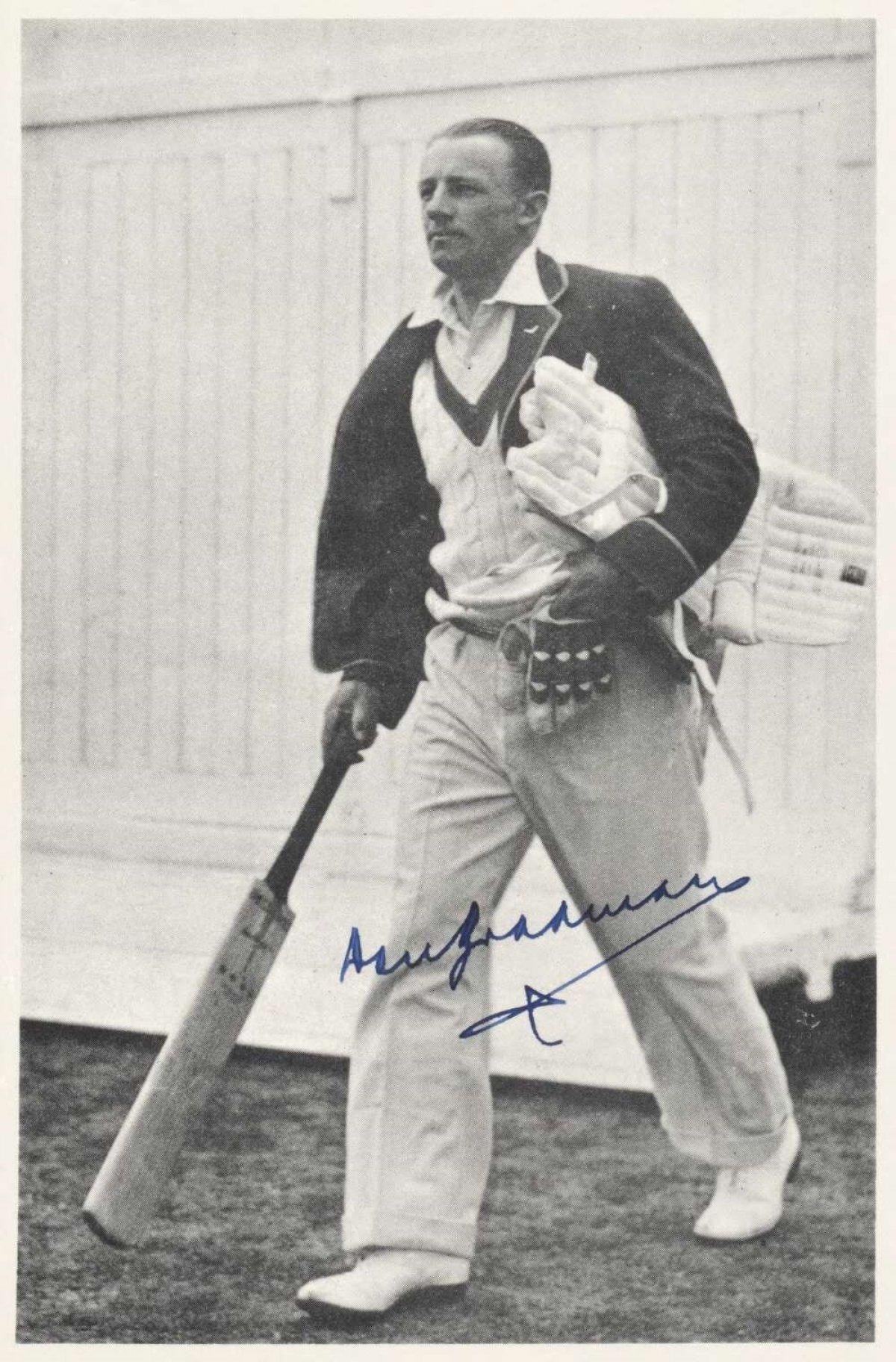 A black and white signed photo of Don Bradman walking onto the oval with his pads and cricket bat.