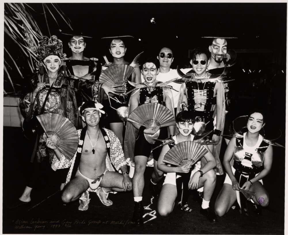 A black-and-white group photo of participants from the Asian Lesbian and Gay Pride Group at the 1994 Mardi Gras. The group wears theatrical costumes with fans and headpieces, posing together with smiling faces, showcasing cultural pride and creative expression.