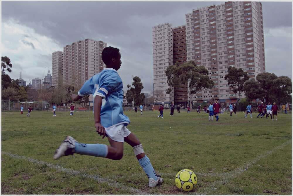 A young boy in a blue soccer shirt, white shorts and soccer boots is about to kick a yellow soccer ball back into the game.