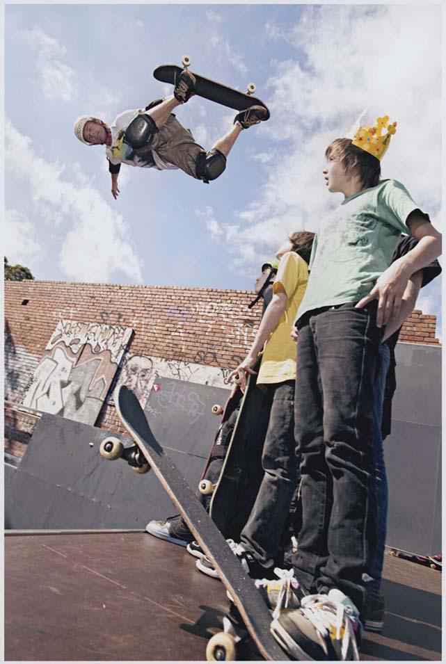 A man in the air doing a trick on a skateboard on the left with some young men watching him on the right