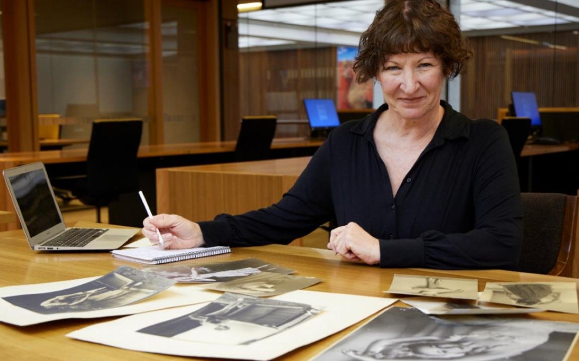 2023 NLA Scholar Yvetter Grant sitting in Library reading room examining old dance photos