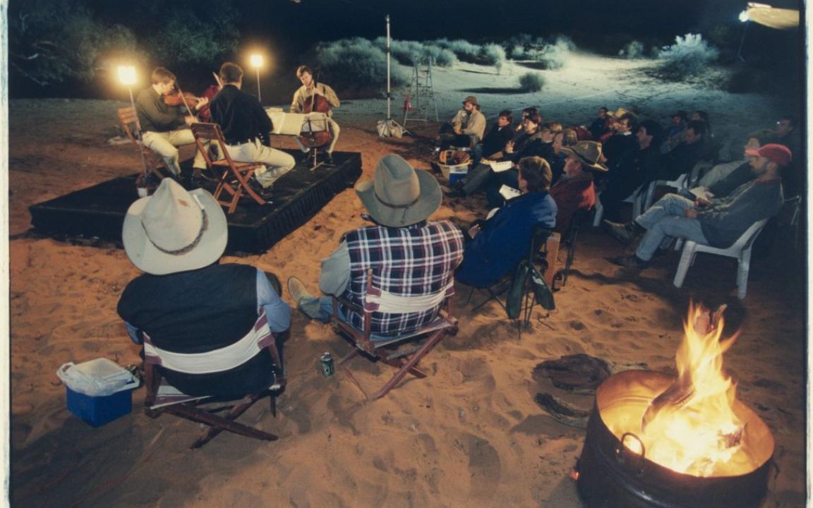 The Australian String Quartet perform on a stage in a dried-up creek bed near the Clayton Station. A small group of audience members are sitting in chairs in front of the stage.