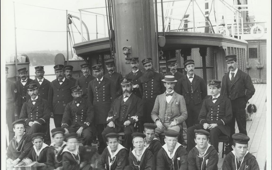 Captain Neitenstein and other male crew/staff of the Sobraon in uniforms and a small group of students sitting on the deck