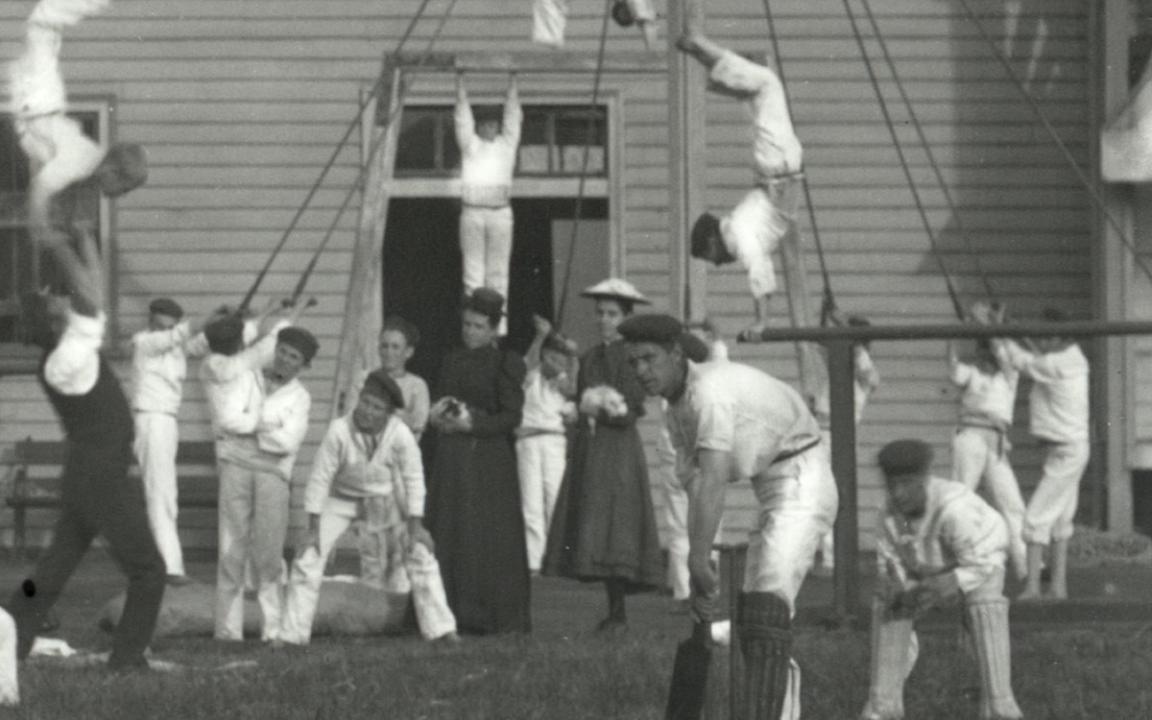 A young girl and a woman standing amongst the students of the Sobraon having recreational time playing cricket and doing gymnastics