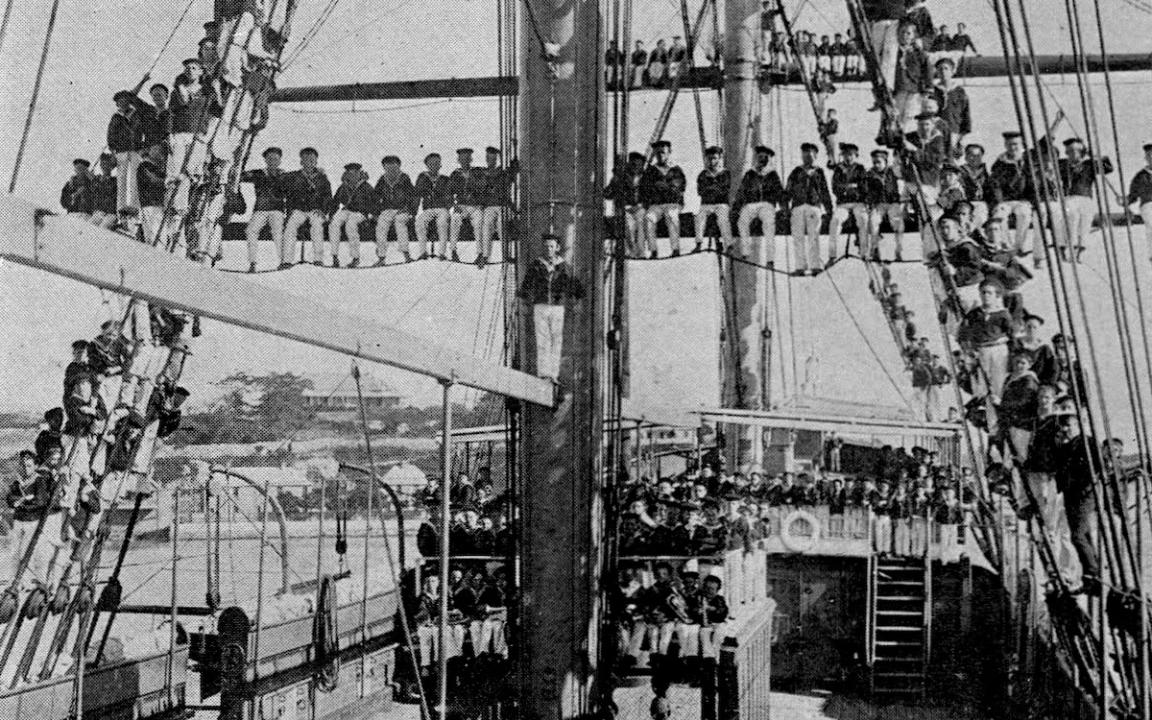 Many school aged children wearing uniforms and sitting on the deck and up on the mast of a ship