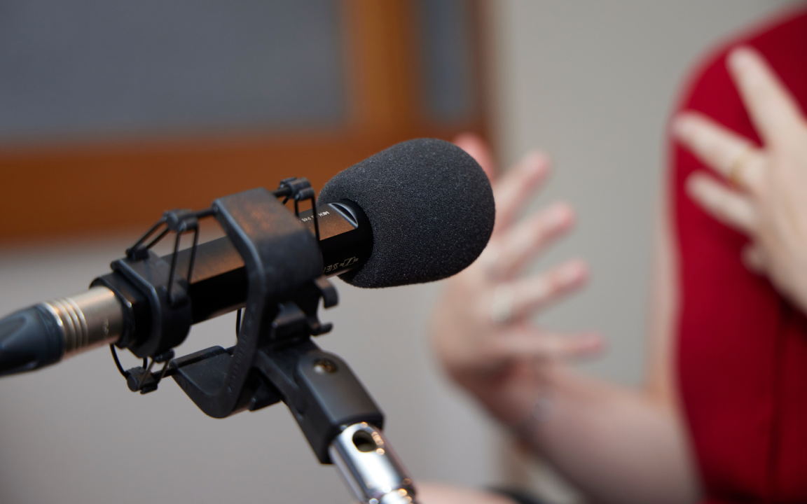 Microphone on a stand pointed towards a woman wearing red speaking and gesturing with her hands