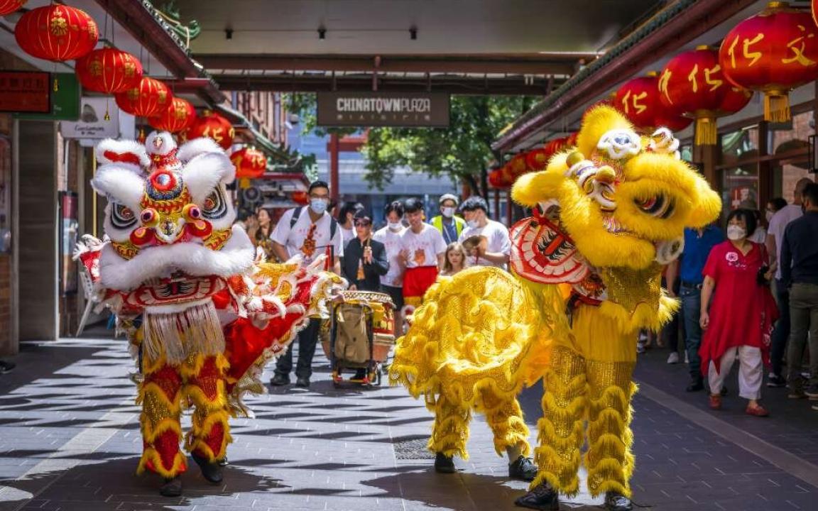 Dancers wearing tradition lion costume performing for Chinese New Year. There are two lions, one red and one yellow, with two people in each costume. Behind them stand spectators and a drummer