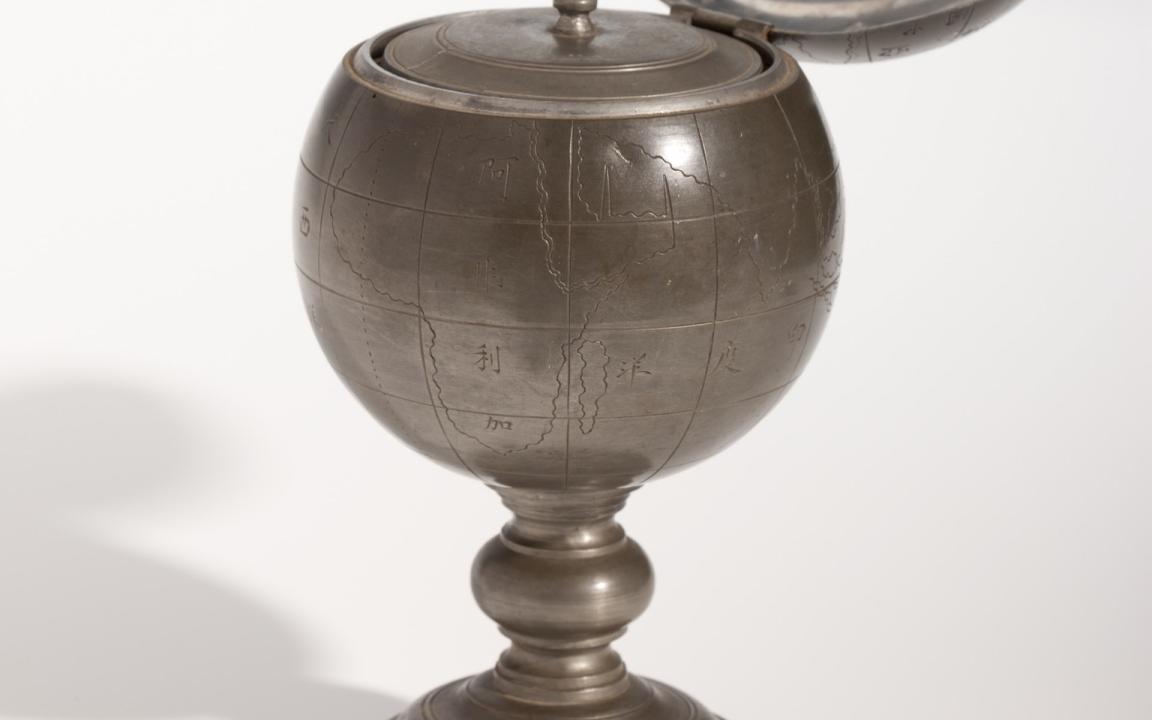 Round pewter tea caddy with a map engraved on it and the lid open