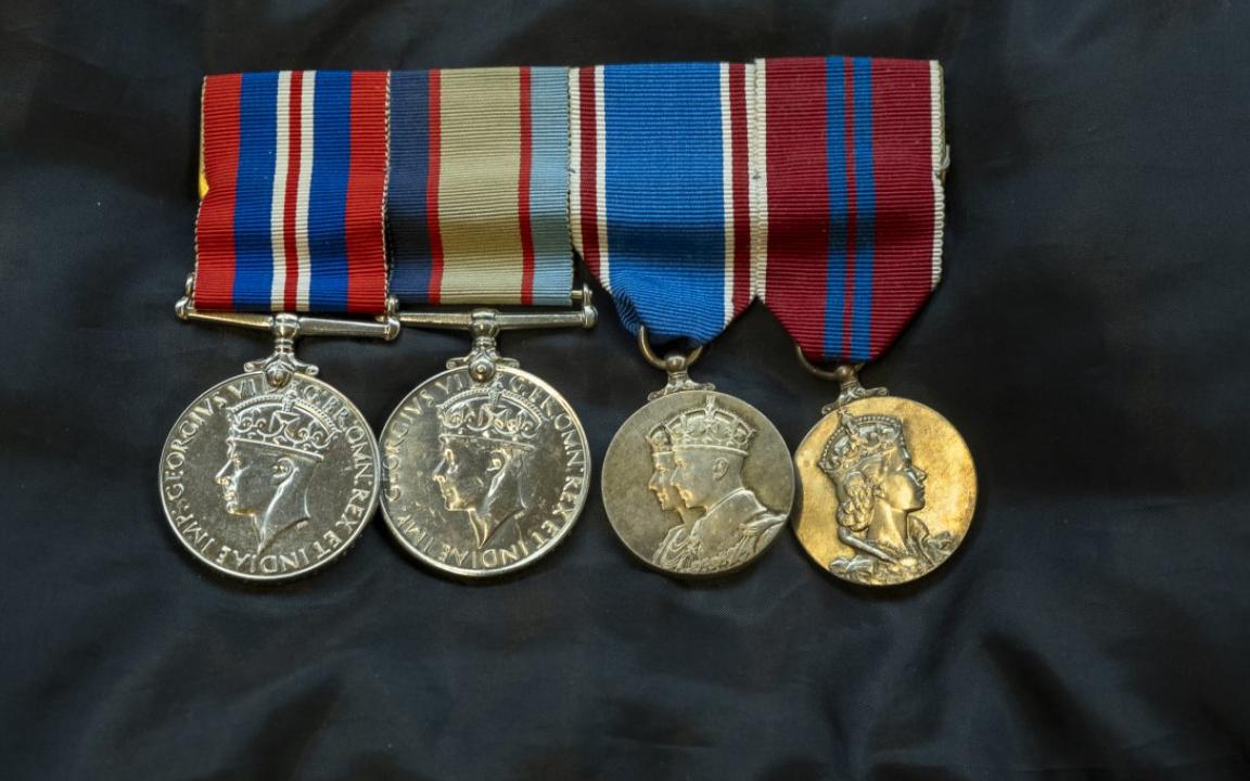 Four medals on a black fabric surface. The ribbons of the medals are various colours, mostly red and blue, and the medals themselves are engraved with a portrait