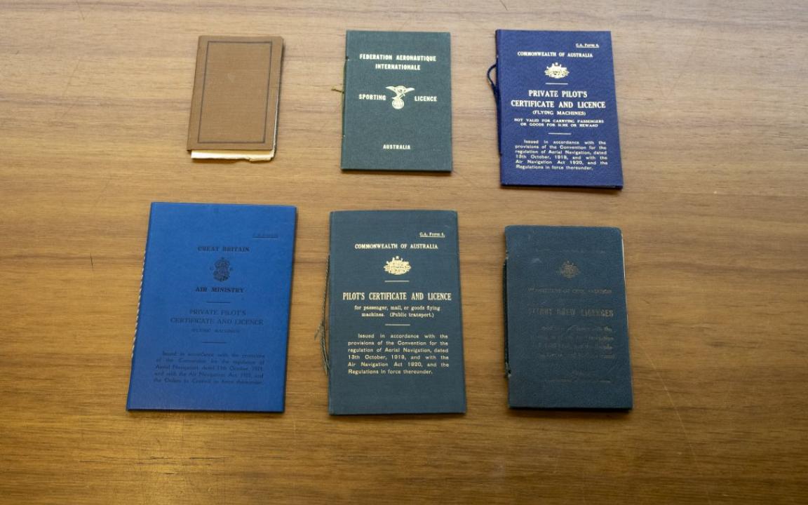 Four small, thin books of various colours (blue, green and brown) sitting on a wooden table