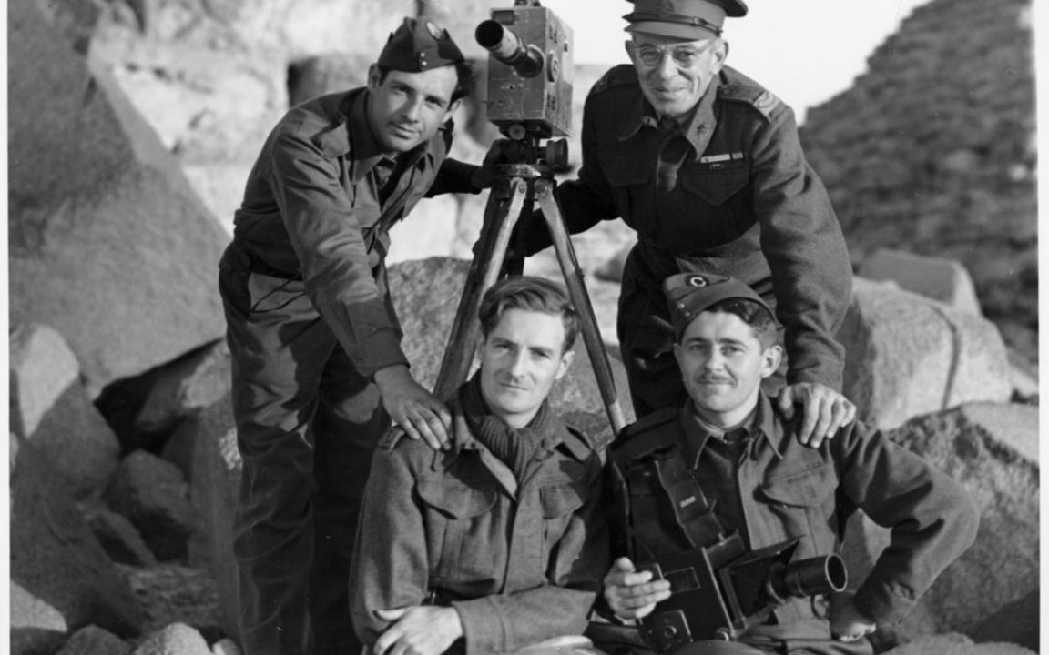 Four men of various ages in military dress around an old video camera