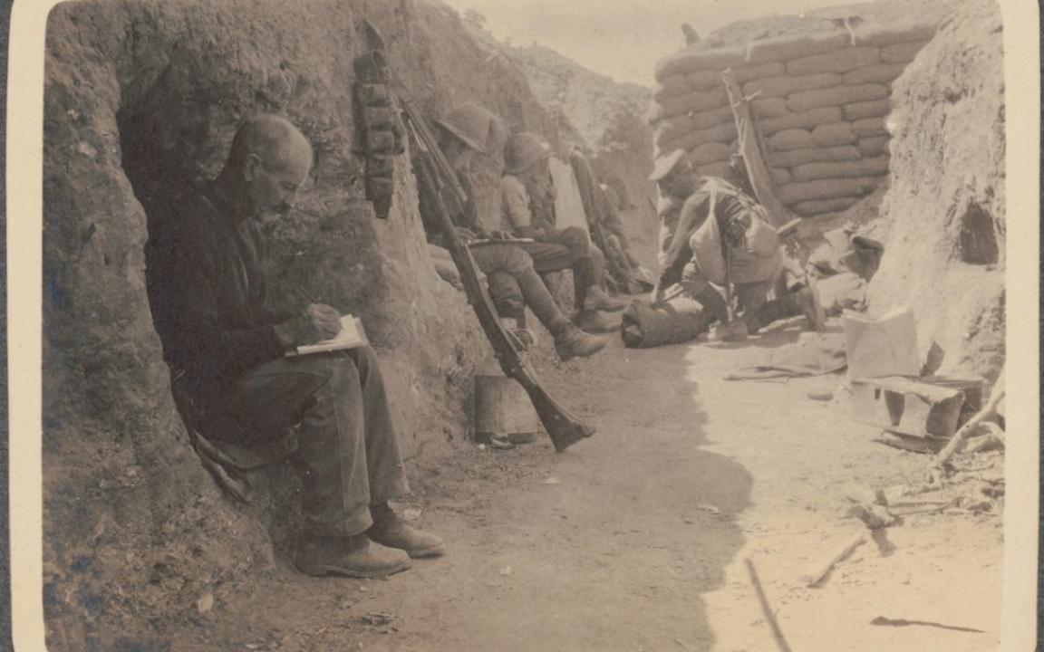 Sepia toned photo of soldiers sitting in a trench writing letters