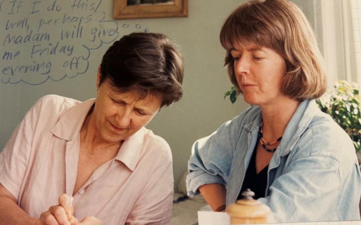 Two women looking down at something out of frame. One is wearing a pink shirt and one is wearing a blue shirt.