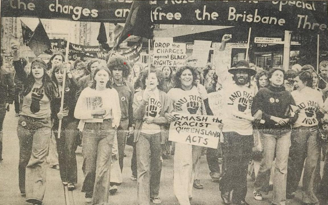 A sepia image of a group of people marching in a protest for Australian First Nations land rights