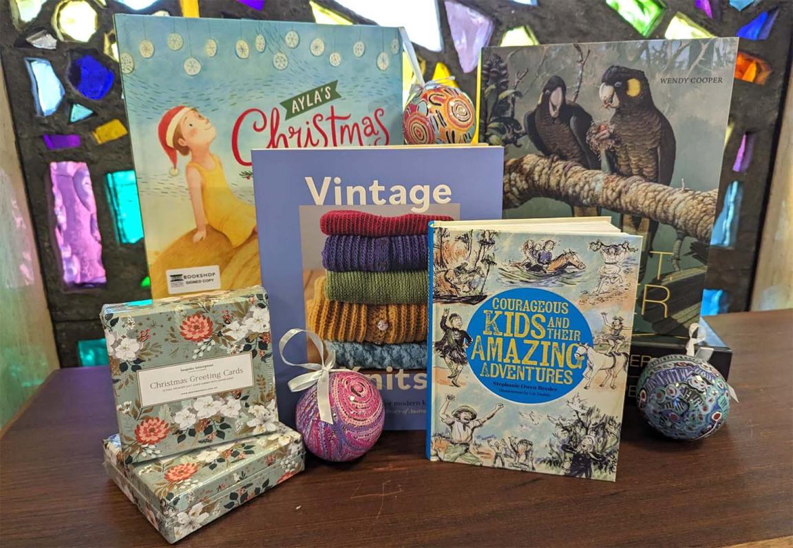 A variety of books and gifts displayed nicely on a table in front of stained glass windows.