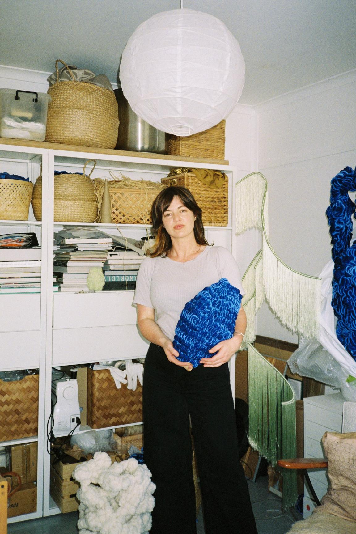 Artist Caro Pattle holding a blue velvet sculpture in an art studio