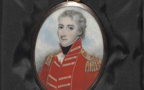 A painted locket portrait of a man in a red military uniform. The locket is resting on some black material.