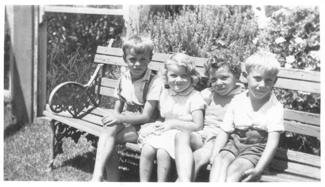 Four young children sitting on a bench and smiling