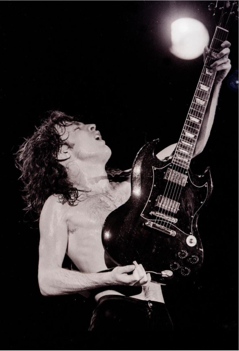 A black and white image of a man with long hair, wearing no shirt, playing guitar