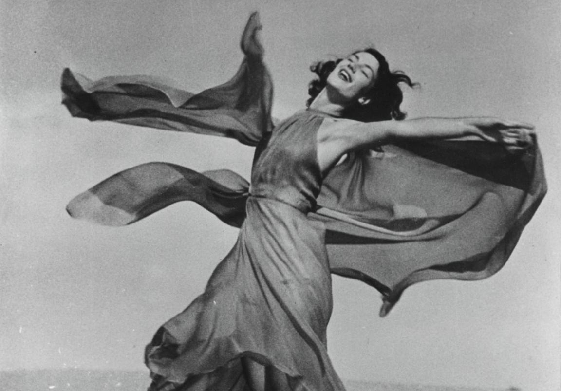 A black and white photograph of a woman in a dress twirling around with her eyes closed.