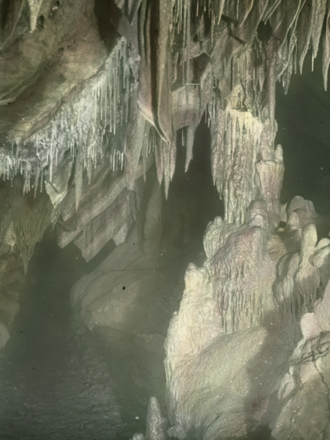 Rocks inside a dark cave. Sharp, pointy rocks come down from the roof of the cave, while rounder, large rocks extend from the ground and sides