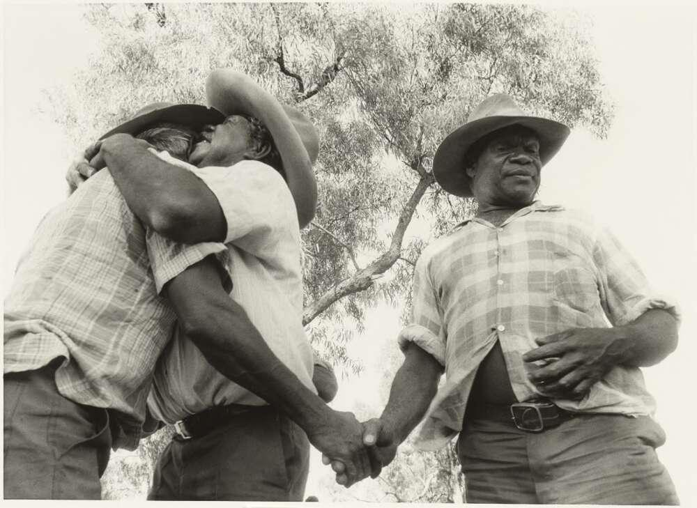 Two men hug and another man shakes one of their hands