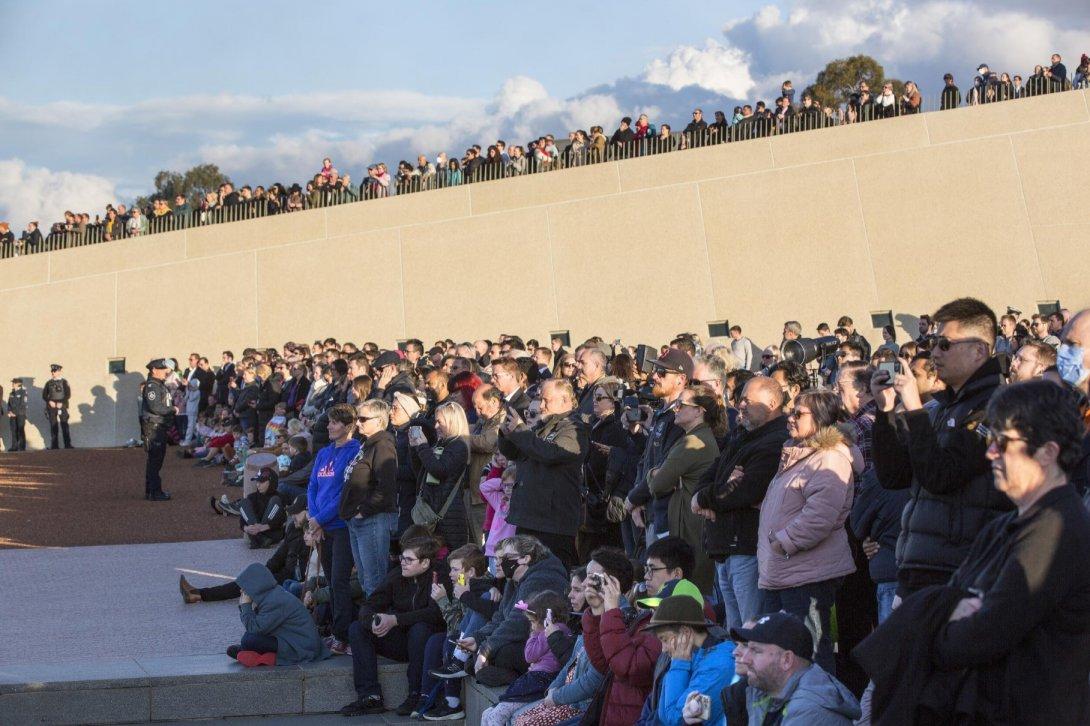 A large crowd of people all standing and looking in the same direction. Some of them are taking photos.