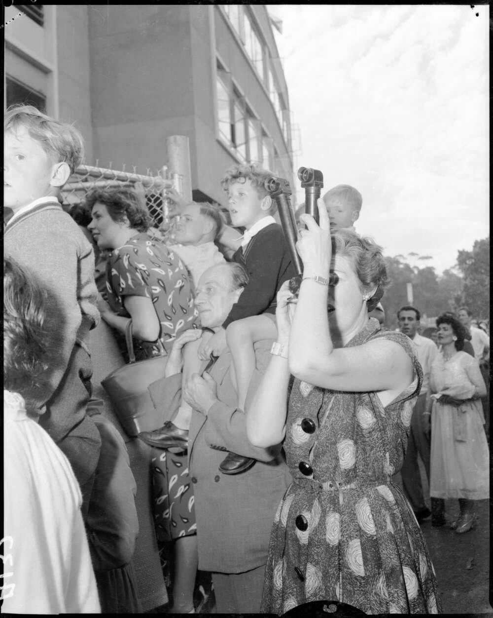 Woman in crowd standing outside sports arena using periscopes to see above the crowd and over the fence