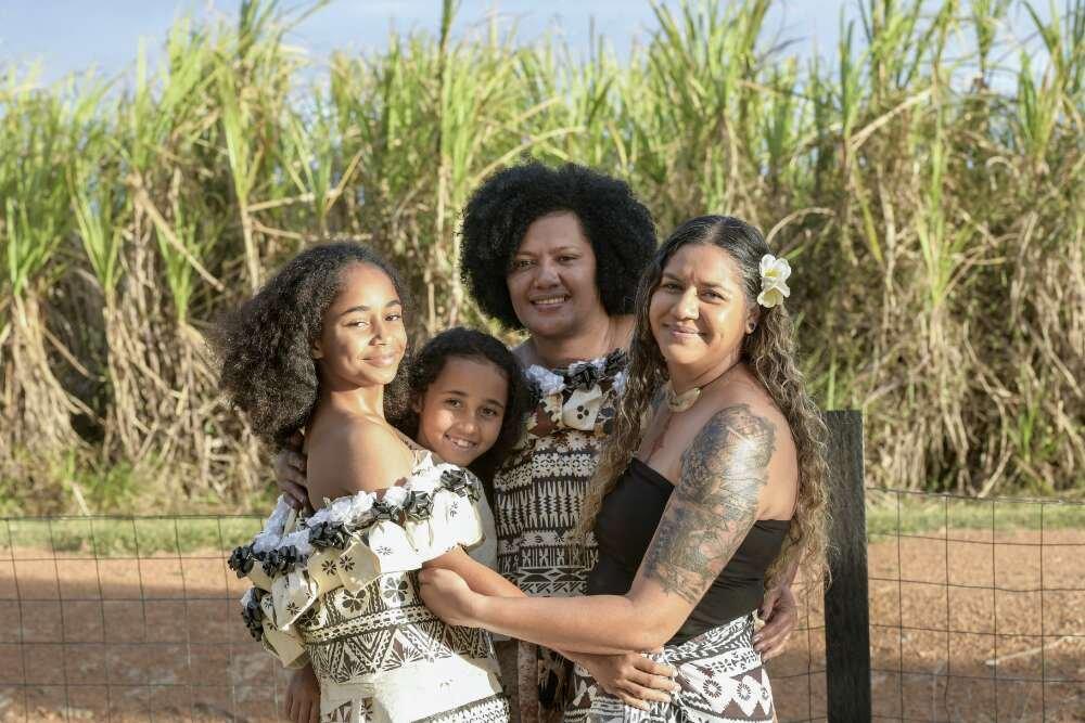 Four Fijian women of various ages wearing dresses smiling and embracing