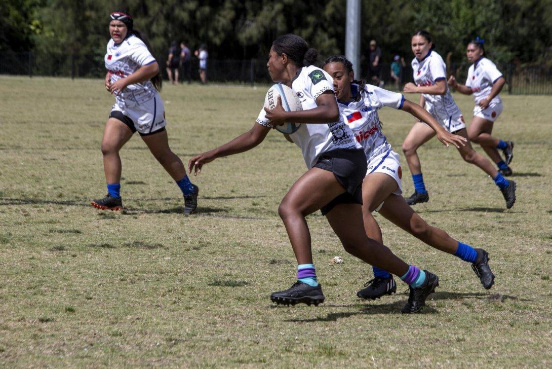 Five girls playing a rugby game on a rugby pitch.