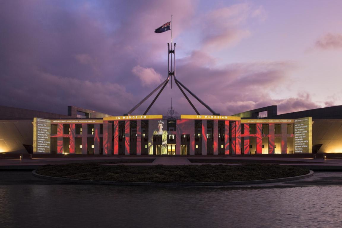 Parliament House at sunset, lit up with an image of Queen Elizabeth II and the words 'In memoriam'.