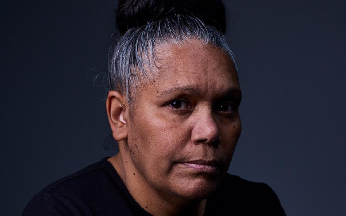 A portrait photo of a woman with her hair tied up in a bun and wearing a black shirt.