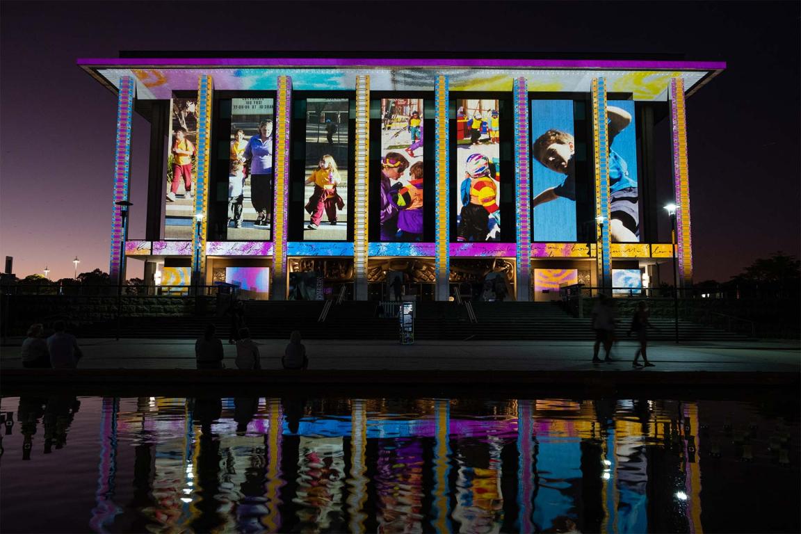 The National Library of Australia building at dusk, lit up with colourful projections.