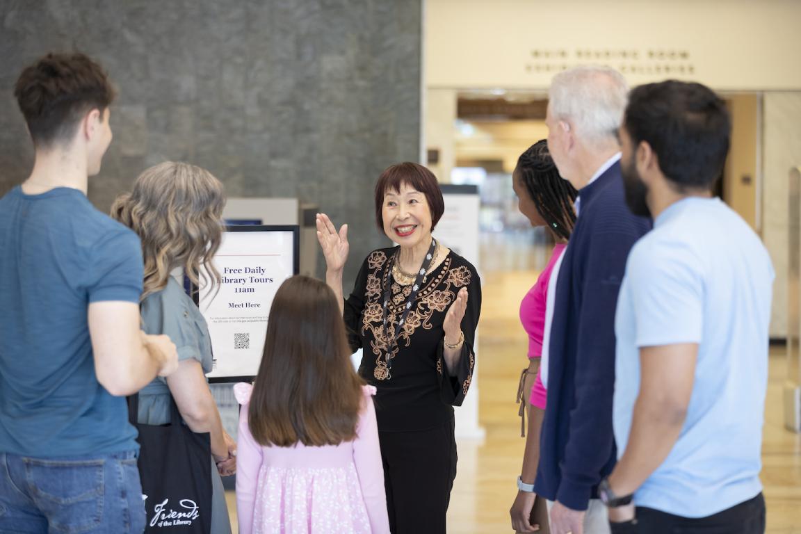 Volunteer Library tour guide smiling and greeting a tour group, made up of people of various ages, in the foyer.