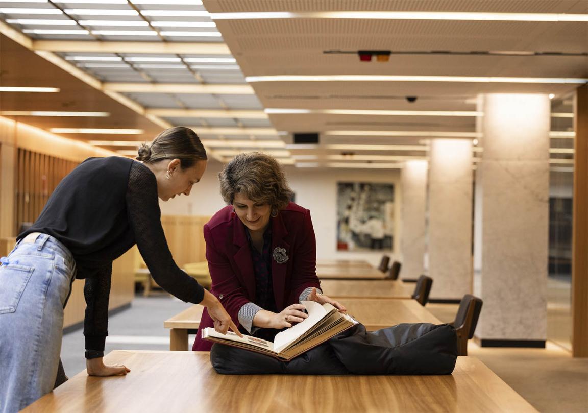 Two people bending over a desk and looking at a book.