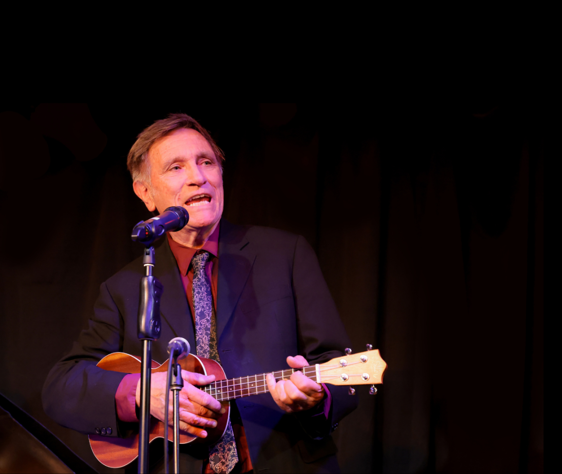 Man in a suit and tie playing guitar and singing behind two microphones