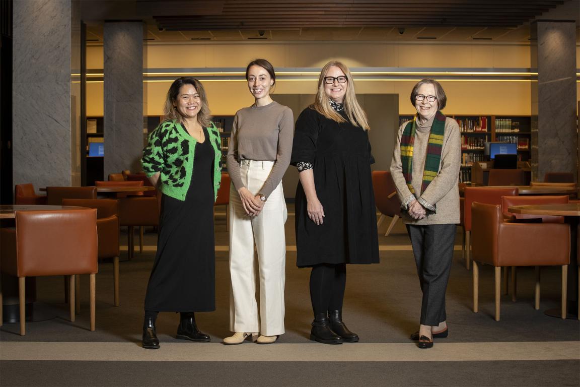 Four people standing in front of chairs and tables.