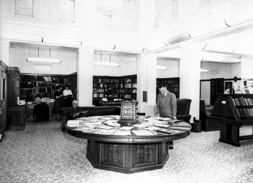 Several people in the Parliamentary Reading Room. One man is looking down at documents on a round table.