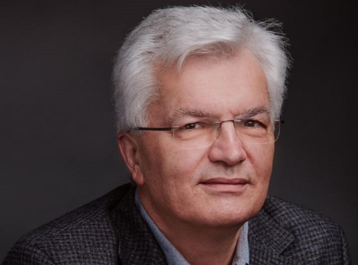 A headshot of a man with white hair and wearing glasses.