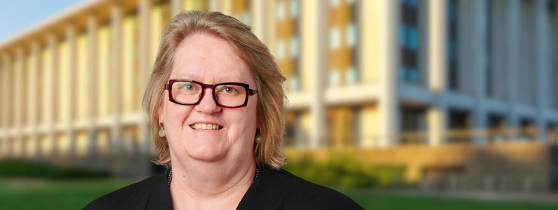 Woman with short blonde hair and dark red square glasses standing in front of the National Library