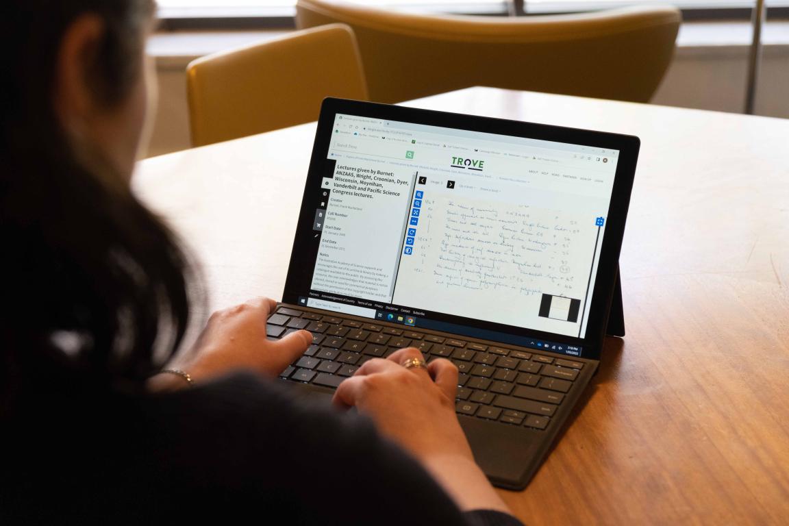 Over the shoulder of woman using laptop. On her screen she is using Trove to look at digitised handwritten notes from a lecture