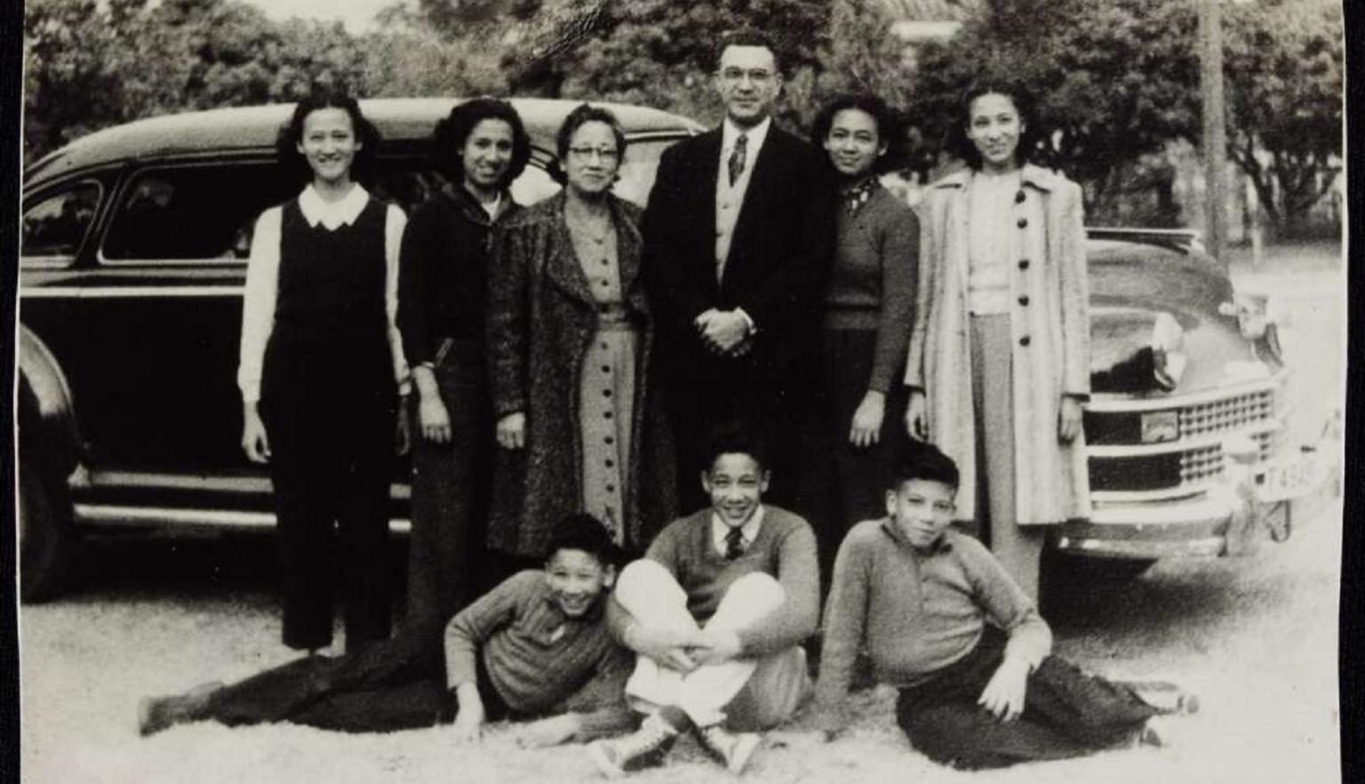 9 members of the Braga family standing in front of a car. 