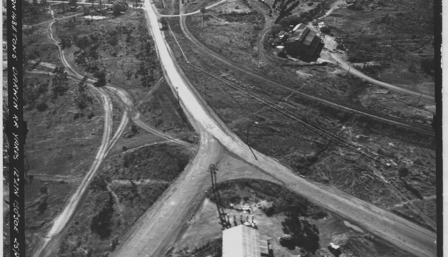 A black and white aerial image of a a main road comes to a fork, there is no traffic and very few buildings. 